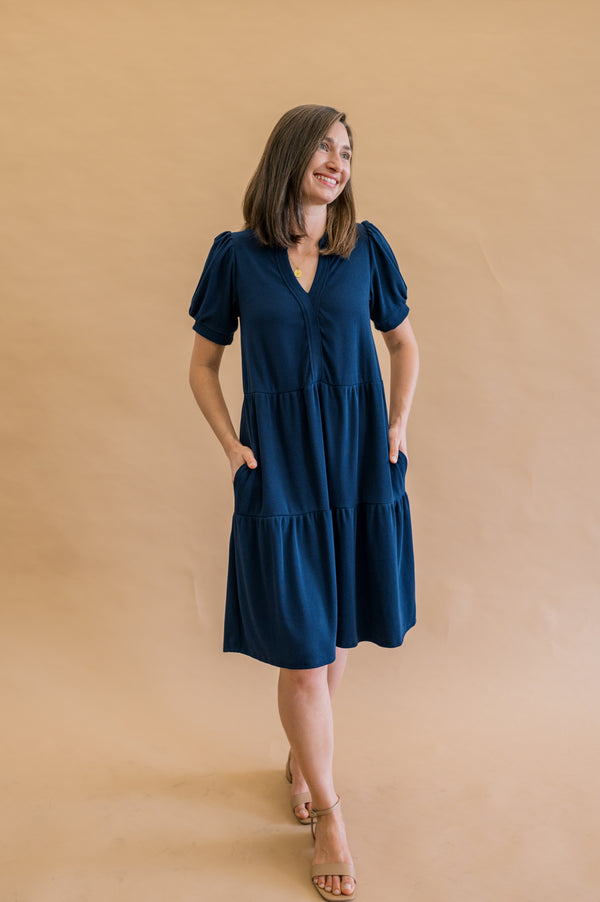 Navy Tiered dress on size XS model. Worn with tan heels, and a comfortable loose fit, puff sleeves and knee length design