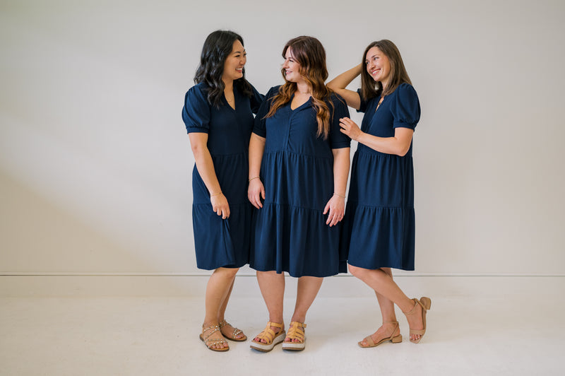 Group photo of our navy tied dress on three sizes. Full coverage knee length short sleeve dress. 