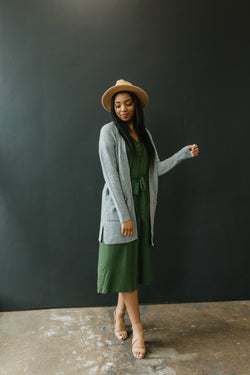 Olive Green Henley Anywhere Dress on model. Model is standing and wearing a grey cardigan and green Anywhere Dress.