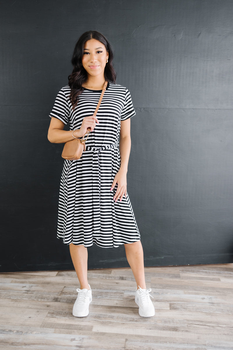 Model wearing anywhere striped knee length dress with waist tie and rolled sleeves.