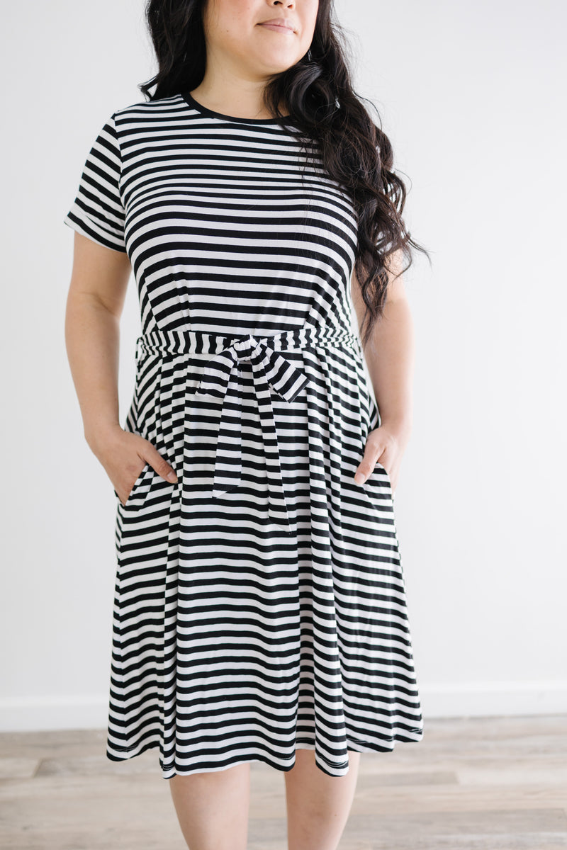 Detail view of stripes and tie on model wearing anywhere striped knee length dress with waist tie and rolled sleeves.