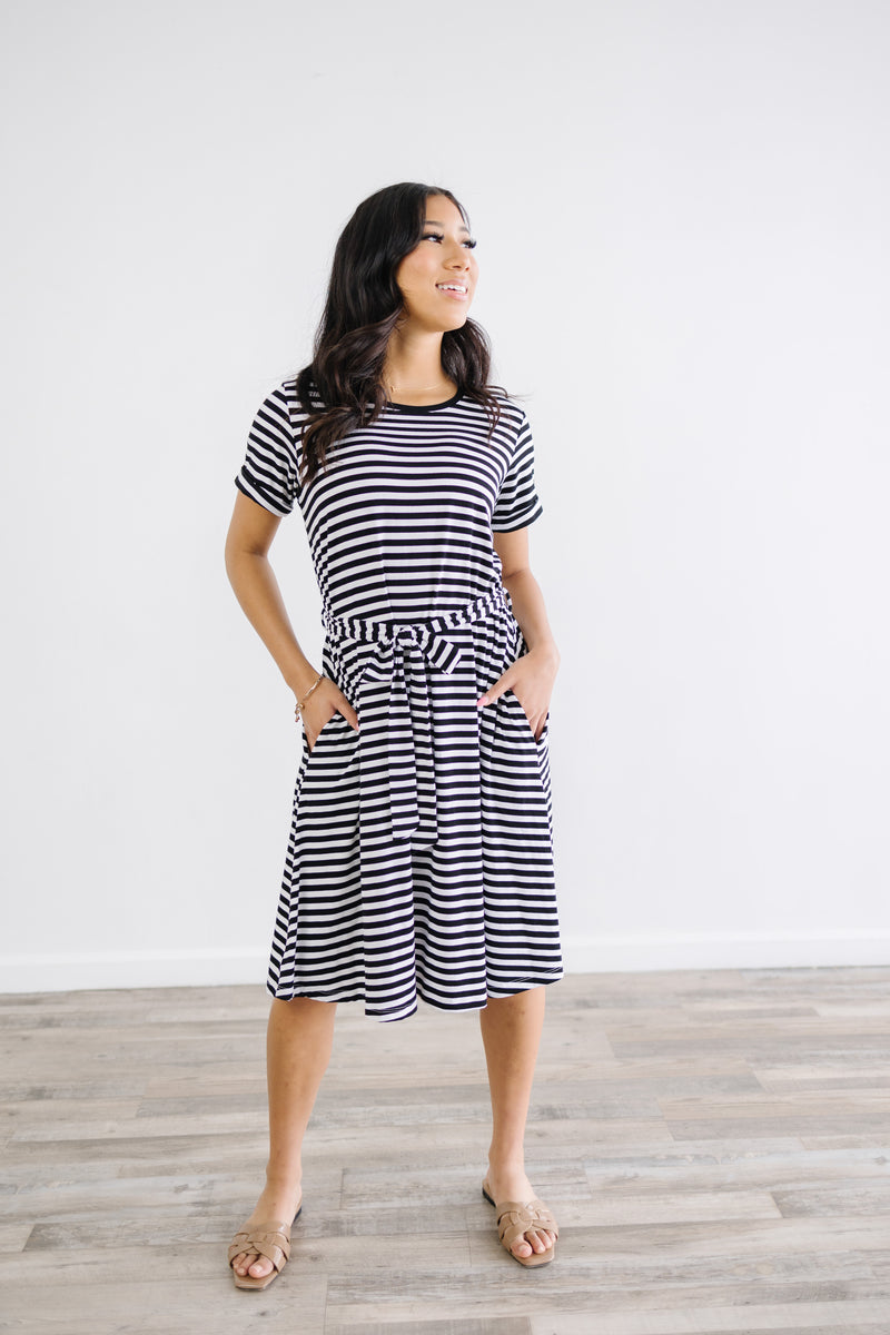 Model wearing anywhere striped knee length dress with waist tie and rolled sleeves.