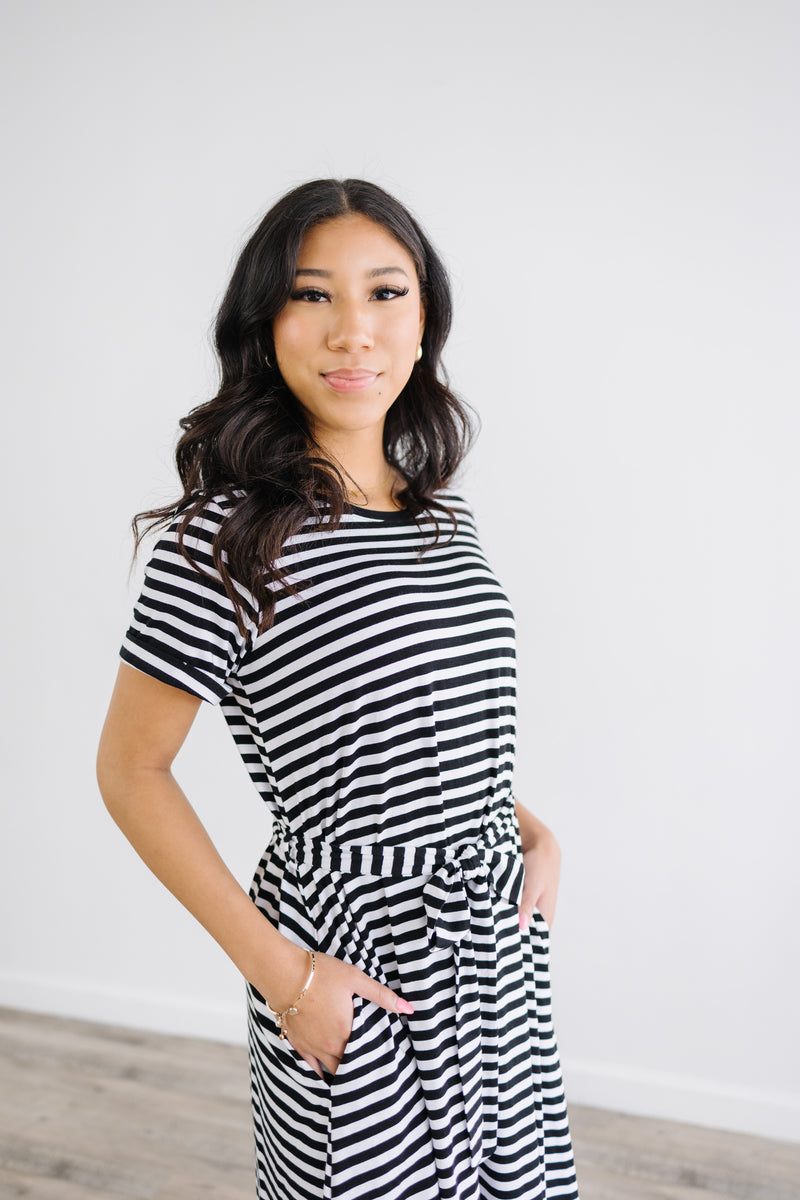 Close up of Model wearing anywhere striped knee length dress with waist tie and rolled sleeves.